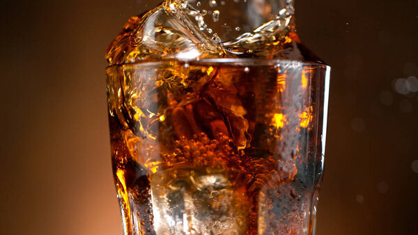Cola pouring in a glass with ice cubes