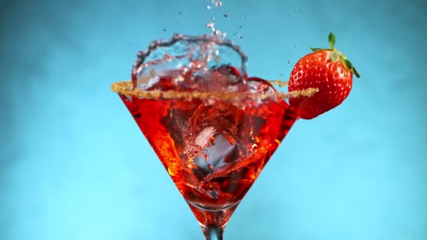 Cocktail lumineux avec glaçon tombant sur fond bleu. — Video