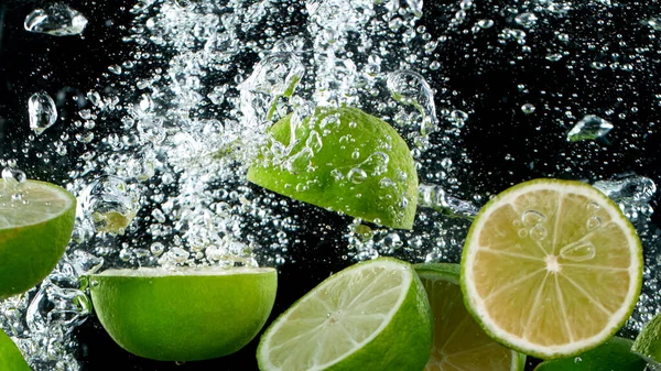 Limas cortadas en rodajas que caen al agua —  Fotos de Stock