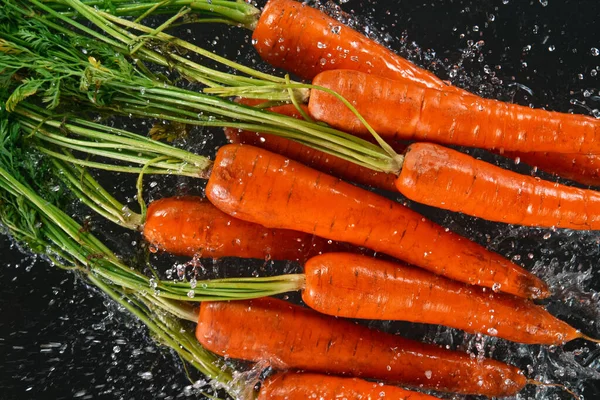 Falling fresh harvested carrots, water splash during impact — Stock Photo, Image