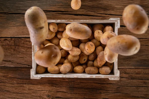 Batatas frescas colhidas caindo em uma caixa de madeira. — Fotografia de Stock