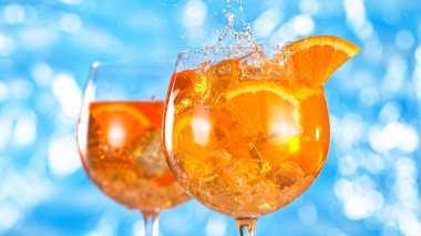 Buz küpü portakal kokteyli bardağına düşüyor. Deniz yüzeyi arkaplanlı Aperol spreyi.