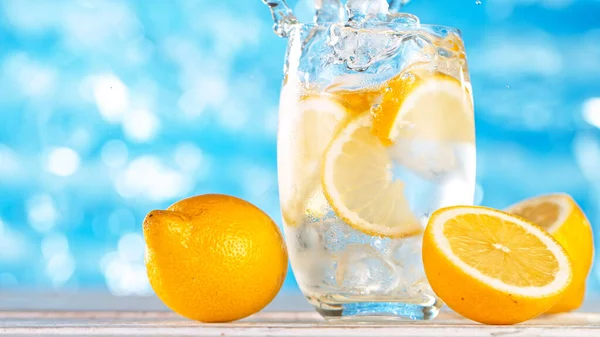 Cubo de gelo caindo em vidro de limonada cítrica com fundo de superfície do mar. — Fotografia de Stock