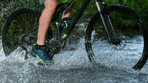 Sportman paardrijden fiets in de ondiepe beek en spetterend water. — Stockfoto