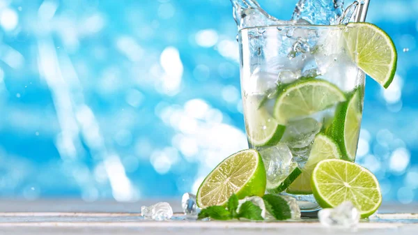 IJsblokje valt in glas mojito cocktail met zeeoppervlak achtergrond. — Stockfoto