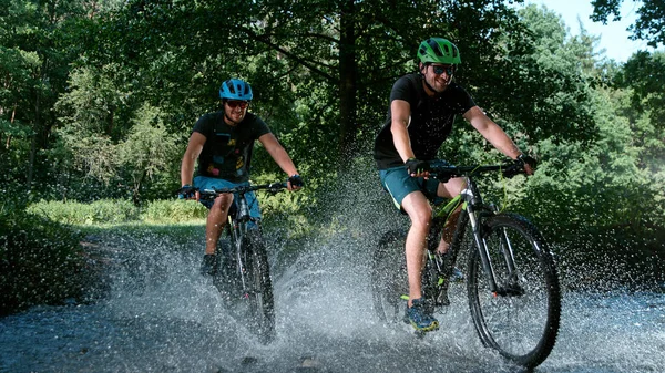 Sportsmen riding bicycles in the shallow stream and splashing water. — Stock Photo, Image