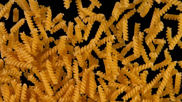 Freeze motion of flying uncooked italian pasta fusilli on black background. — Stock Photo, Image