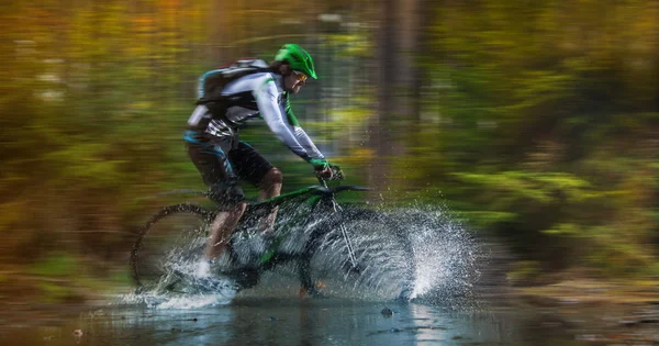 Ciclista de montaña corriendo a través del arroyo forestal . — Foto de Stock