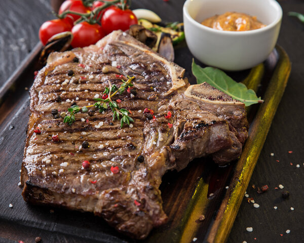 Beef t-bone steak on black stone table, close-up.