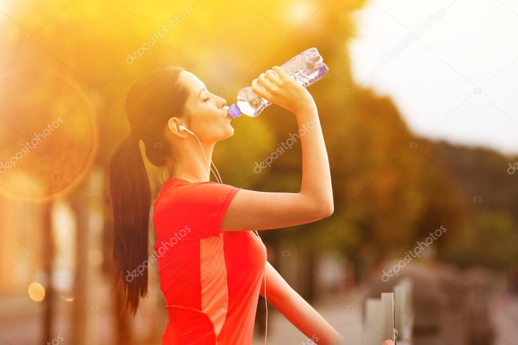 Young woman drinking water after running in the city.