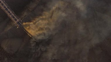 Aktif bir kömür madenciliğinin hava görüntüsünde havaya yükselen ağır makineler ve duman görülüyor