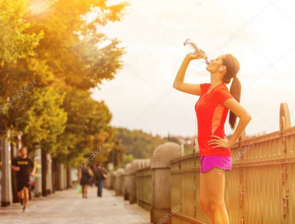 Young woman drinking water after running in the city