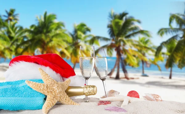 Champagne flutes with santa cap on sunny beach. — Stock Photo, Image