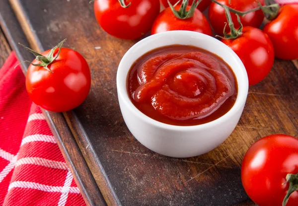 Misku s rajčatovou omáčkou a cherry rajčátky na dřevěný stůl. — Stock fotografie