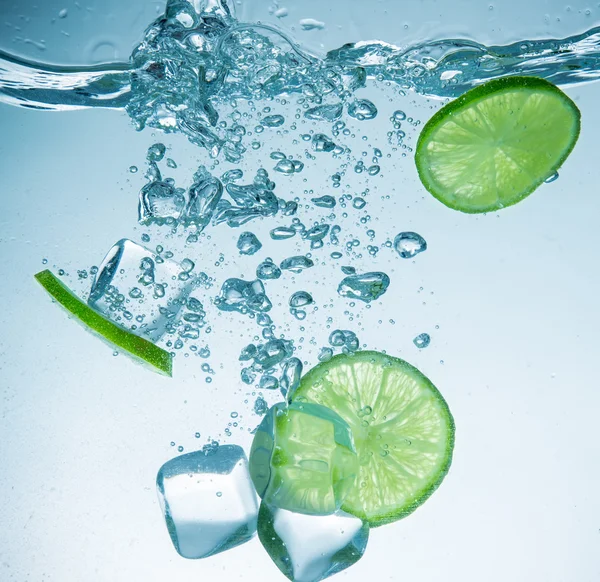 Limes with water splash and ice cubes — Stock Photo, Image