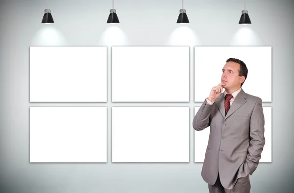Homem de negócios pensando de pé na galeria com seis moldura em branco — Fotografia de Stock
