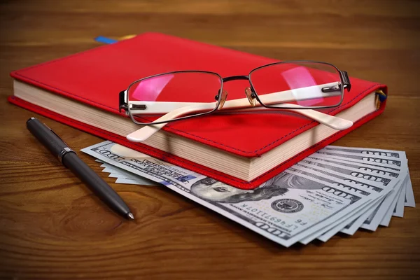 Diário vermelho, óculos, caneta e dólares — Fotografia de Stock