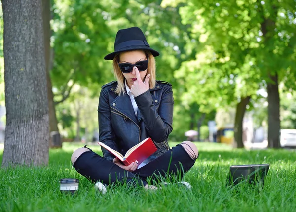 Gelukkig hipster meisje zittend op het gras met boek en laptop — Stockfoto