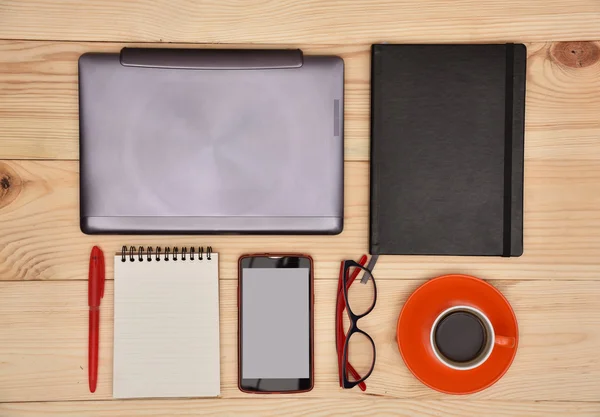 Gesloten laptop, mobiel, bril en kopje koffie op houten tafel — Stockfoto