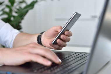 Akıllı telefon tutan ve dizüstü bilgisayarda yazan bir tüccar. İletişim ve ticaret konsepti. Kapat.