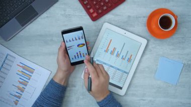 Tüccar akıllı telefon ve dijital tablet ekranının hisse senedi raporunu analiz ediyor. Finans ve Ticaret Konsepti.
