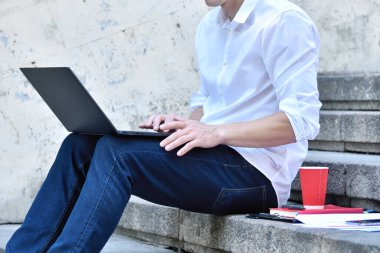 Tüccar merdivenlerde oturuyor ve dizüstü bilgisayarda yazıyor. Finans ve ticaret konsepti. Kapat.