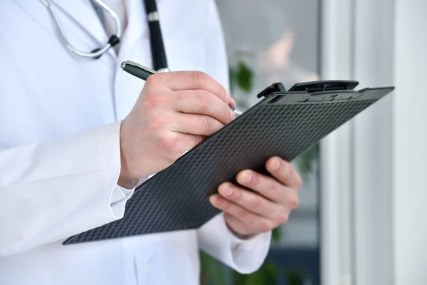 Male doctor standing with black clipboard in clinic. Healthcare and medicine concept.