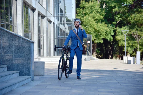 Businessman in helmet with bike talking on mobile phone. Business and alternative transport concept.