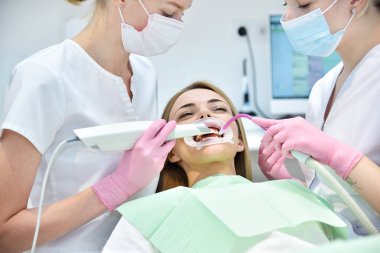 Diş hekimi ve asistanı 3D tarayıcıyla hastanın dişlerini fırçalıyor. Sağlık ve stomatoloji kavramı