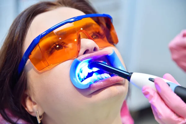 Woman having teeth whitened by dental UV whitening device. Teeth whitening procedure  concept. Close up