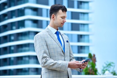 Modern gökdelen arka planında akıllı telefon kullanan bir iş adamı. İş ve teknoloji kavramı.