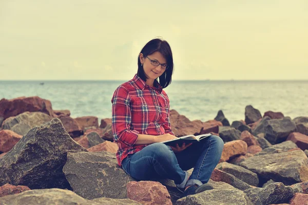 Meisje, zittend op een rots en lezen van een boek — Stockfoto