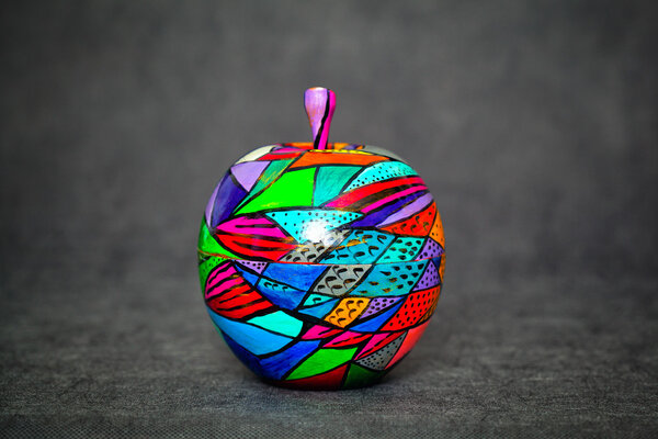 Декоративное деревянное яблоко на темном абстрактном фоне, окрашенные цвета. тема ручной работы
