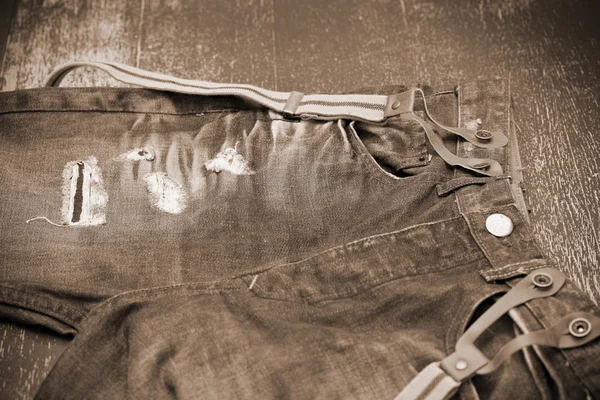 Holey jeans with suspenders, photo toning in sepia — Stock Photo, Image