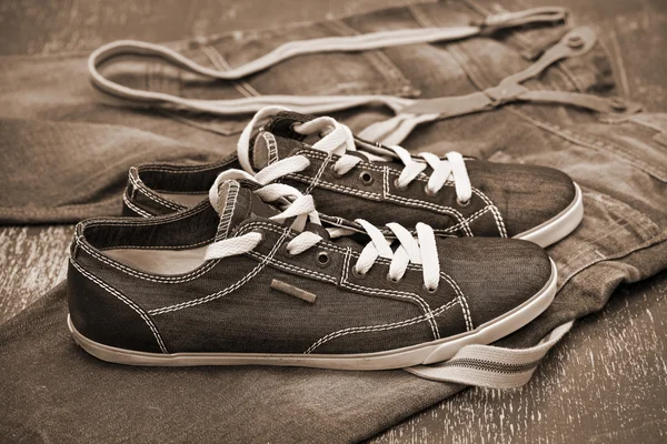 Zapatillas negras y jeans con tirantes. Foto tonificación en sepia — Foto de Stock