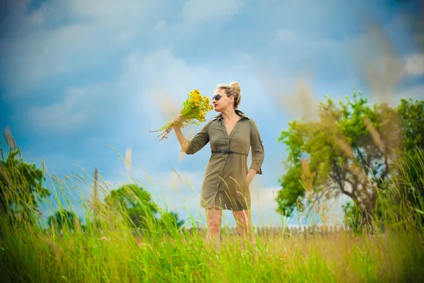Menina bonita em vestido verde na aldeia cheirando um buquê de flores amarelas — Fotografia de Stock