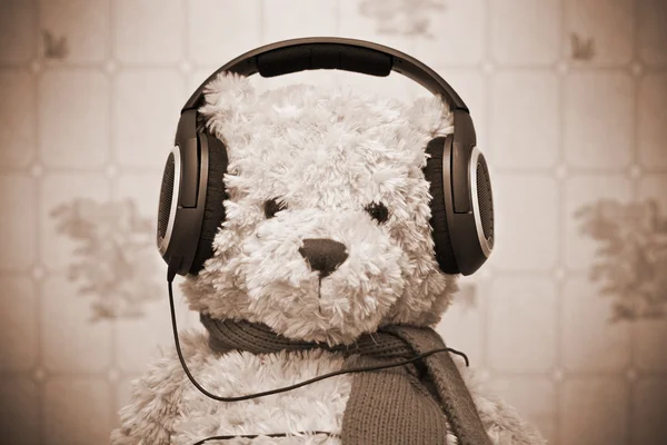 Osito de peluche escuchando música en los auriculares. Foto de sepia tonificada, estilo retro — Foto de Stock