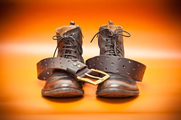 Autumn still life: men's leather shoes and a leather belt with a buckle. Fashion boots and belt of brown color on a red background — Stock Photo, Image