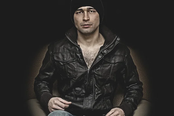 Brutal man in a hat and leather jacket on a black background — Stock Photo, Image