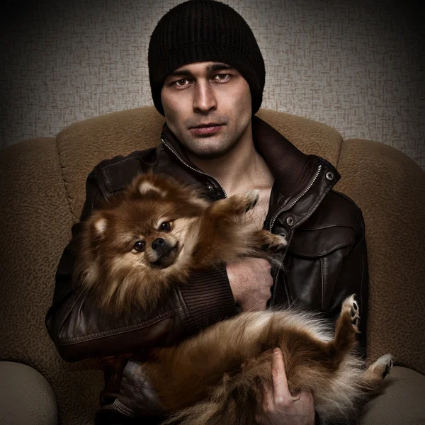 Brutal man in a hat and leather jacket with a dog in her arms — Stock Photo, Image