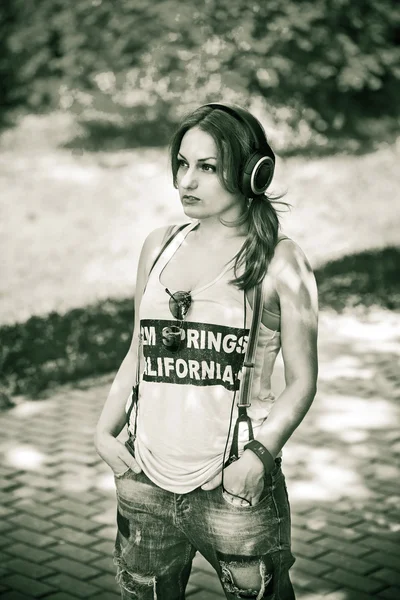 Portret pięknej młodej dziewczyny na zewnątrz w dżinsy i t-shirt, słuchanie muzyki na słuchawkach — Zdjęcie stockowe