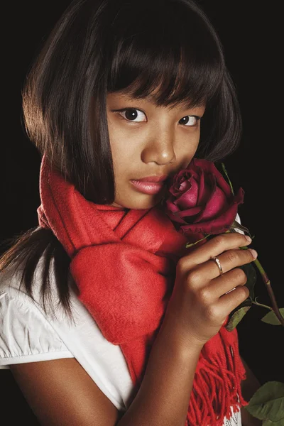 Studio portrait of a girl of Asian ethnicity in a red scarf with burgundy rose in her hand — Stock Photo, Image