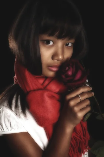 Beautiful brunette girl in a red scarf around his neck, with a red rose in her hand on a black background — Stock Photo, Image