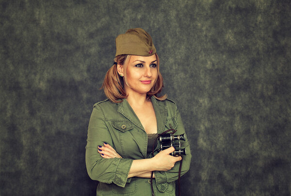 Улыбающаяся девушка в гарнизонной фуражке с военным биноклем со времен Второй мировой войны на абстрактном тёмном фоне. Инсценировка к празднику Победы 9 мая
.