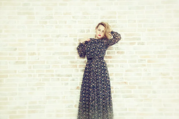 Beautiful girl in a long dress against a background of a brick wall — Stock Photo, Image