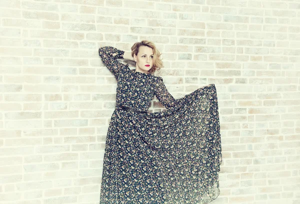 Beautiful woman lifted the hem of her dress and posing against a brick wall background — Stock Photo, Image