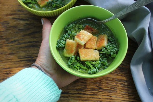 Mano de mujer sosteniendo sopa verde fresca y deliciosa. Cuenco de brócoli con croutons. Concepto alimenticio de desintoxicación dietética. Vista superior, plano —  Fotos de Stock