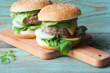 Biftek, soğan, salatalık, marul, peynir, ıspanak ve baharatlı ev yapımı hamburger. Tahta kesme tahtasına yakın taze hamburger. .