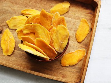 Ahşap kasede kurutulmuş mango şeritleri. Dilimlenmiş, susuz mango. Sarı ve turuncu renkli sulu tropikal taş meyveler.