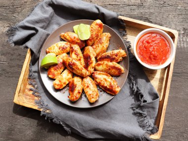 Kireç ve ahşap tepside kırmızı soslu baharatlı tavuk kanatları.